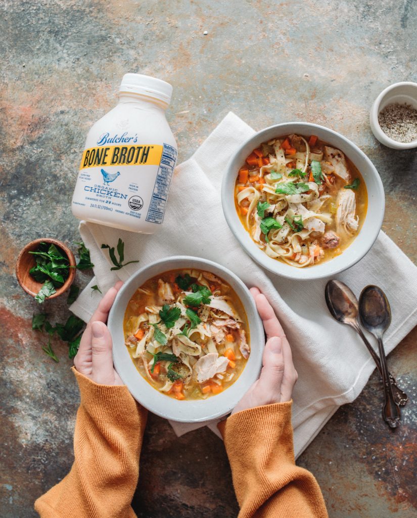 Bone Broth Soup being held by two hands next to a bottle of bone broth