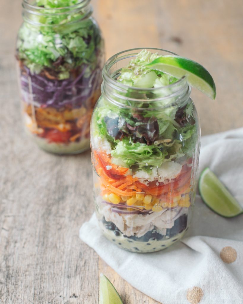 A colorful Southwestern Chicken Mason Jar Salad next to a slice of lime